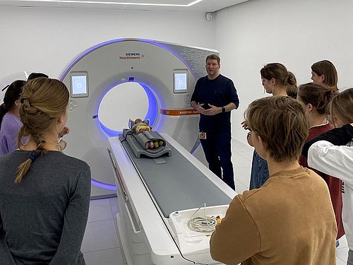 Ein Gruppe von Schülerinnen steht um ein CT. Ein Ausbilder erklärt die Funktionsweise.