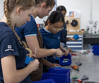 Eine Gruppe von Mädchen steht an der Werkbank und montiert das Werkstück zusammen