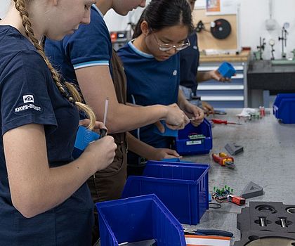 Eine Gruppe von Mädchen steht an der Werkbank und montiert das Werkstück zusammen