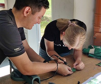 Ein Auszubildender hilft einem Mädchen beim Löten 