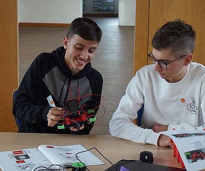2 Jungen sitzen vor einem Tisch und bauen Plastikteile zu einem Roboter.