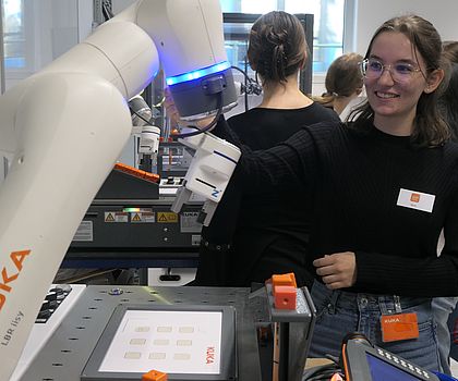 Man sieht ein Mädchen das lacht während sie mit dem  Roboterarm von KUKA arbeitet. 