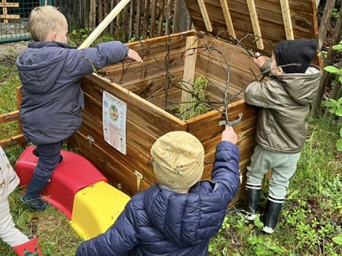 Das Foto zeigt Kinder, die etwas in eine große Kompostkiste werfen.