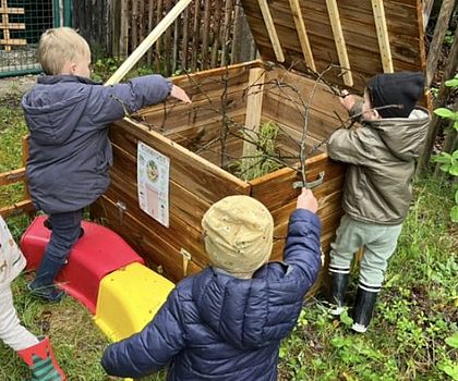 Das Foto zeigt Kinder, die etwas in eine große Kompostkiste werfen.