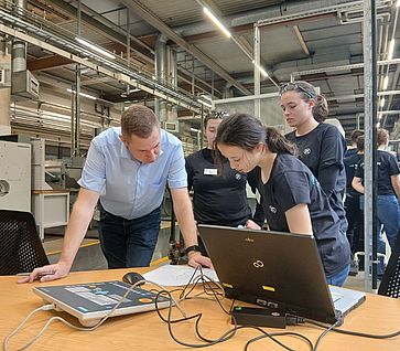Ein Ausbilder betrachtet zusammen mit einem Mädchen die Ergebnisse auf einem Laptop