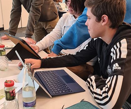 3 Jungen sitzen vor einem Tablet und arbeiten am Projektauftrag