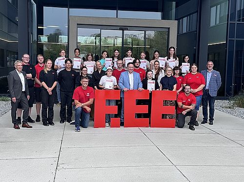 Gruppenbild der Teilnehmerinnen des Mädchen für Technik-Camps mit Ehrengästen und Betreuenden vor großen roten F.EE-Buchstaben.