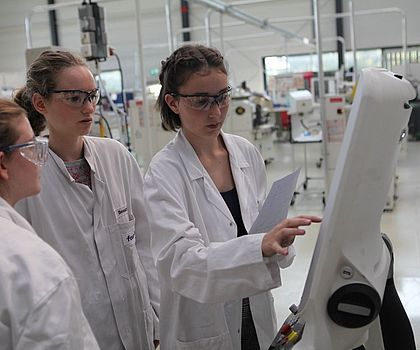 drei Mädchen stehen vor einer Programmiermaschine in weißen Kitteln