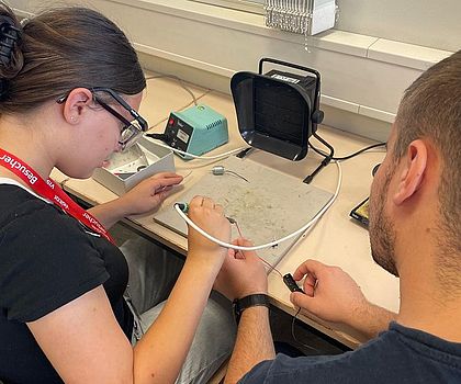 Ein Mädhcen erhält Unterstützung beim Löten von einem Auszubildenden