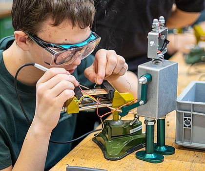 Ein Junge lötet Kabel an die Hülle des Roboters.