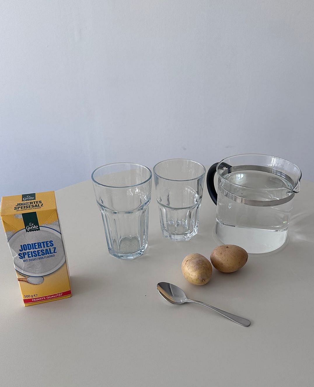 Man sieht die Material für unser Experiment:2 gleich große Gläser, Löffel, Salz, Warmes Wasser, 2 Kartoffel, so groß, dass sie gut in die Gläser passen