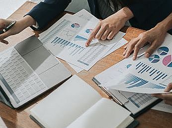 Wirtschaftsmathematik Auf einem Tisch liegen Zettel mit Statistiken. 2 paar Hände analysieren die Statistiken