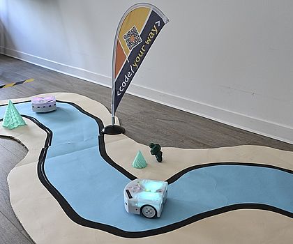 Lernroboter Thymio auf einem Bodenparcours mit schwarzer Fahrspur.