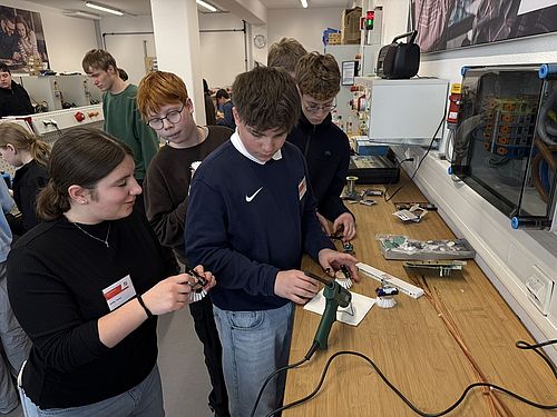 Eine Gruppe von Jugendlicher steht vor einer Werkbank. Alle haben Bürsten in der Hand