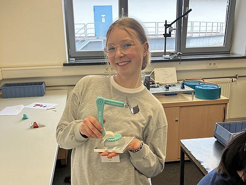 Forscherinnen-Camp bei SGL Carbon und der Hochschule Augsburg Eine Teilnehmerin hält ihre selbstgebaute Handyhalterung aus Carbon, welche wie ein Roboterarm ausschaut, in der Hand