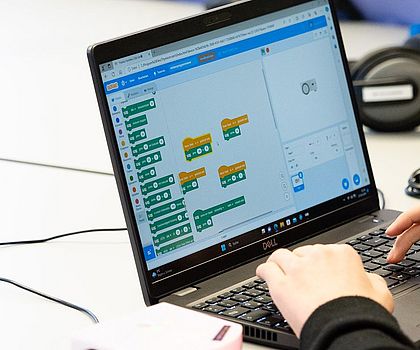 Person programmiert einen kleinen Lernroboter mit grafischer Software am Laptop.