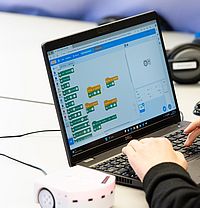 Person programmiert einen kleinen Lernroboter mit grafischer Software am Laptop.