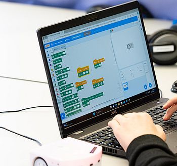 Person programmiert einen kleinen Lernroboter mit grafischer Software am Laptop.