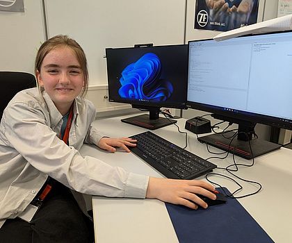 Ein Mädchen sitzt vor einem PC und lächelt in die Kamera