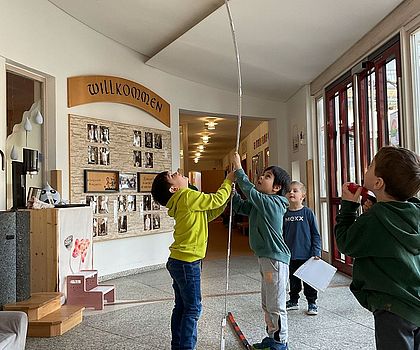 Auf dem Foto sind Kinder zu sehen, die die Raumhöhe der KiTa ausmessen um herauszufinden, ob ein Monstertruck-Reifen hineinpassen würde.
