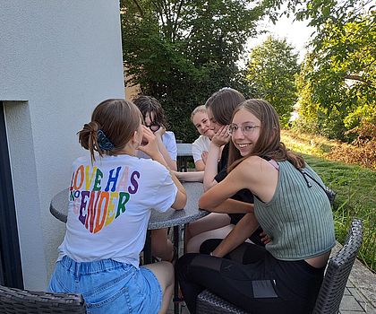 Man sieht eine Gruppe Mädchen draußen um einen Tisch sitzen. 