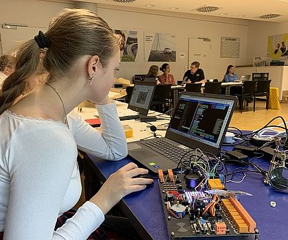 Ein Mädchen sitzt vor einem Laptop. Vor ihr liegt ein Mainboard