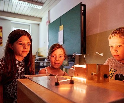 drei Kinder experimentieren im Klassenzimmer mit heißem Draht. ein kleiner Rauch ist zu sehen