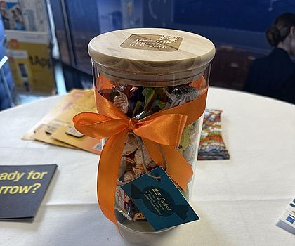 Ein gefülltes Bonbonglas steht auf dem Stich. Drumherum liegen Flyer und Postkarten