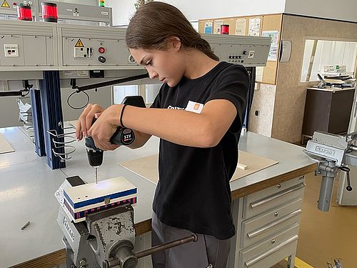 Mädchen für Technik-Camp bei Bosch Rexroth AG In einem Schrabustock ist eine Holzkiste eingespannt. Ein Mädchen steht davor und bohrt Löcher in die Kiste