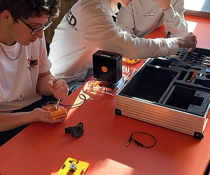 3 Jungen sitzen an einem Tisch. Auf dem Tisch stehen Experimentierstationen.