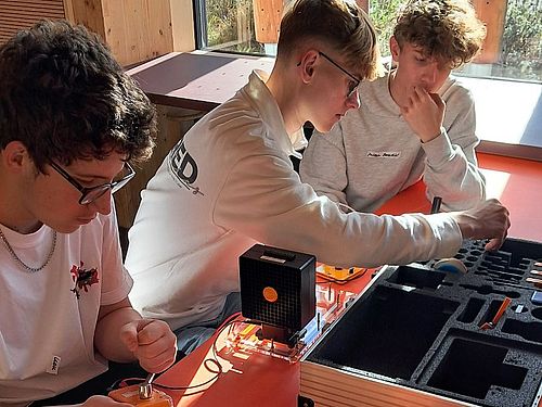 3 Jungen sitzen an einem Tisch. Auf dem Tisch stehen Experimentierstationen.