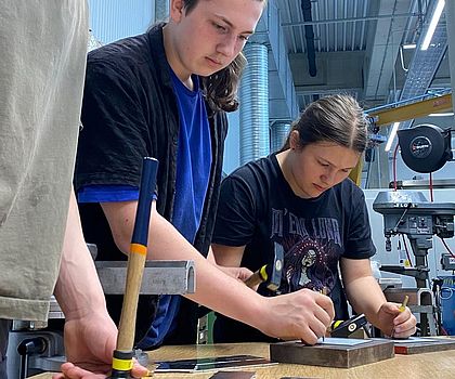 Ein Mädchn und 2 Jungen bereiten Bohrstellen mit Hilfe eines Körners vor.