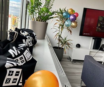 Man sieht ein Fensterbrett auf welchem schwarze Turnbeutel mit der Aufschrift "MINT" liegen und einen orangenen Lutballoon.