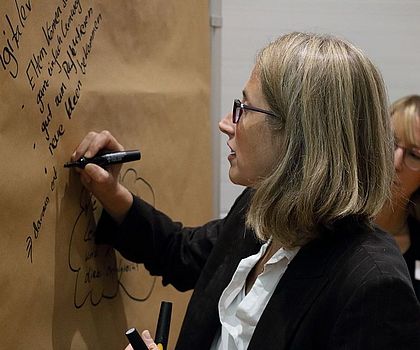 Auf dem Bild ist die Projektleiterin von Es funktioniert?!, Ingrid Nolting, zu sehen.  Sie schreibt auf ein Brown-Paper im Rahmen eines World-Cafe´s Stichpunkte auf.