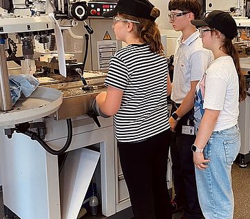 Zwei Mädchen mit Schutzbrillen stehen an einer großen Fräsmaschine in einer Lehrwerkstatt.