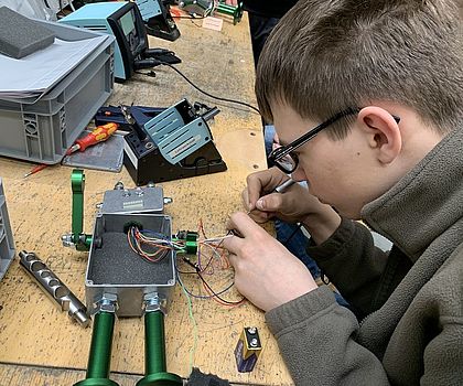 Ein Junge lötet Kabel an einen Metallroboter