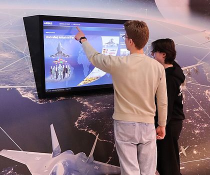 2 Jugendliche stehen vor einem Bildschirm auf den Flugzeuge von Airbus präsentiert werden