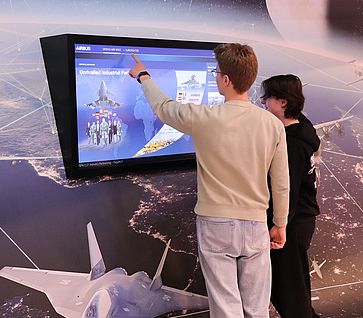 2 Jugendliche stehen vor einem Bildschirm auf den Flugzeuge von Airbus präsentiert werden