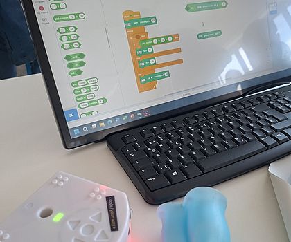 Laptop mit Programmieroberfläche und Lernroboter auf einem Tisch.
