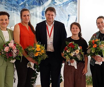 4 Frauen halten jeweils einen Blumenstrauß. Ein Mann steht mittig platziert zwischen ihnen