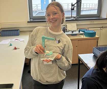 Eine Teilnehmerin hält ihre selbstgebaute Handyhalterung aus Carbon, welche wie ein Roboterarm ausschaut, in der Hand