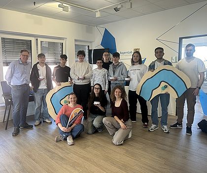 Gruppe von Teilnehmenden mit selbst gestalteten Projektarbeiten in einem Workshopraum.