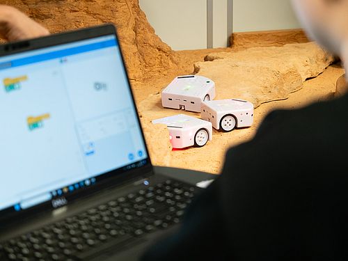 Person programmiert kleine Roboter mit grafischer Software vor einer Testlandschaft.