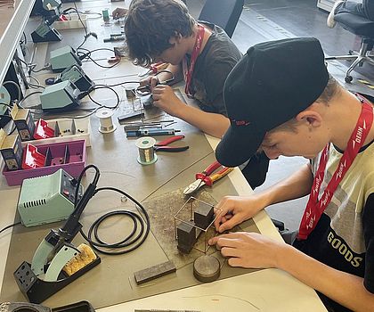 Jugendliche sitzen an einer Werkstattbank und führen Lötübungen durch