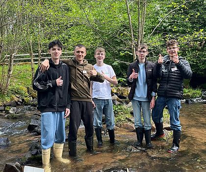 5 Jungen stehen im Bachlauf und probieren die Funktion ihres Papp-Wasserrads aus