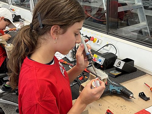 Camp-Teilnehmerin lötet konzentriert elektronische Bauteile an einer Werkbank.