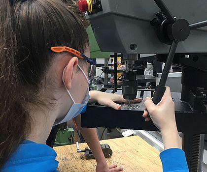 Ein Mädchen bohrt mit einer Standbohrmaschine Löcher in das Werkstück