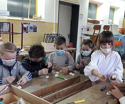 Auf dem Bild ist ein Werkraum zu sehen. Um eine Werkbank herum stehen Kinder, die  versuchen, aus Tischtennisbällen ein Jo-Jo zu basteln.