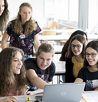 Man sieht mehrere Mädchen, die freudig auf einen Laptop in der Mitte zeigen. 