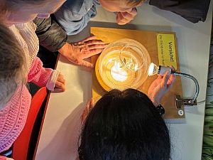 Kinder und Erwachsene beugen sich über eine leuchtende Glühbirnen-Experimentierstation der MINIPHÄNOMENTA. 